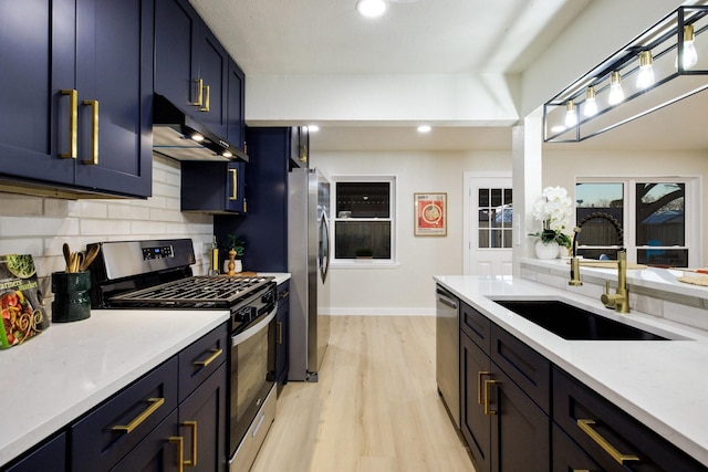 kitchen with light wood-style flooring, under cabinet range hood, a sink, appliances with stainless steel finishes, and backsplash