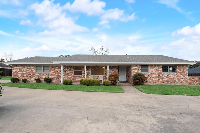 ranch-style home with brick siding, roof with shingles, covered porch, and a front yard