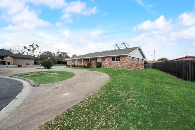 ranch-style house featuring fence, curved driveway, a front lawn, and brick siding