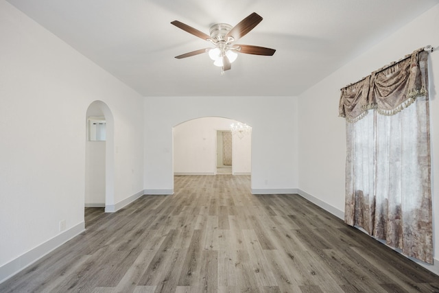 empty room featuring ceiling fan with notable chandelier, arched walkways, wood finished floors, and baseboards