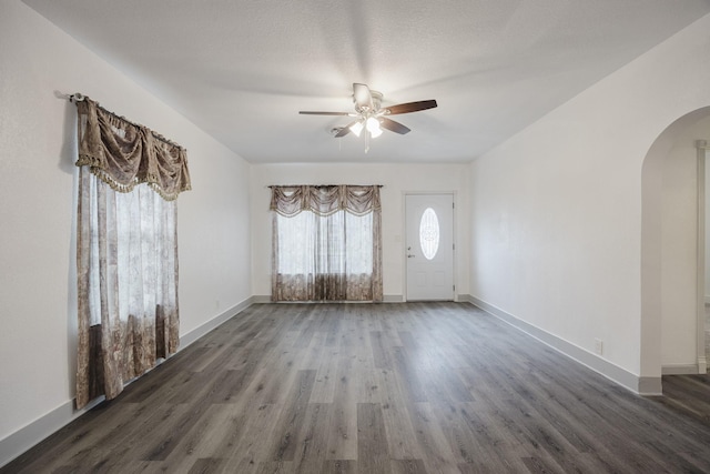 interior space featuring baseboards, arched walkways, ceiling fan, and wood finished floors