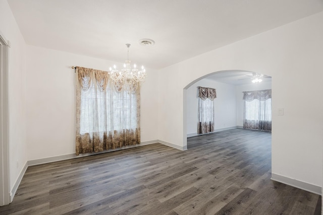 empty room featuring baseboards, visible vents, arched walkways, and wood finished floors