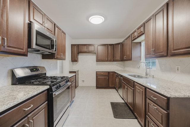 kitchen with light tile patterned flooring, a sink, appliances with stainless steel finishes, decorative backsplash, and light stone countertops