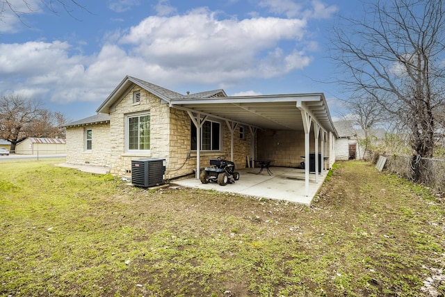 back of house featuring a lawn, a patio, stone siding, a fenced backyard, and central AC