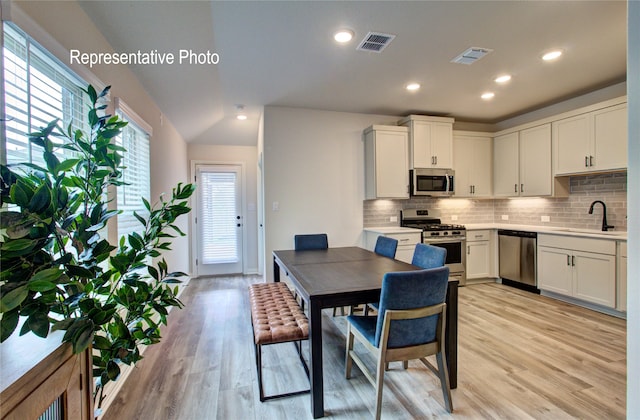 kitchen featuring light wood finished floors, visible vents, a sink, stainless steel appliances, and backsplash