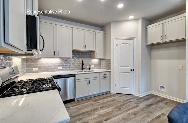 kitchen featuring light wood-style flooring, a sink, appliances with stainless steel finishes, backsplash, and light stone countertops