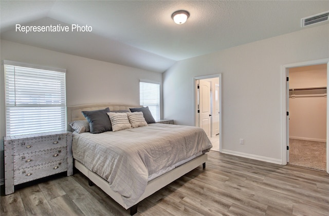 bedroom featuring lofted ceiling, light wood-style flooring, visible vents, baseboards, and a walk in closet