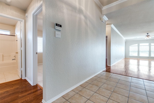 hall with a textured wall, light tile patterned flooring, crown molding, and baseboards