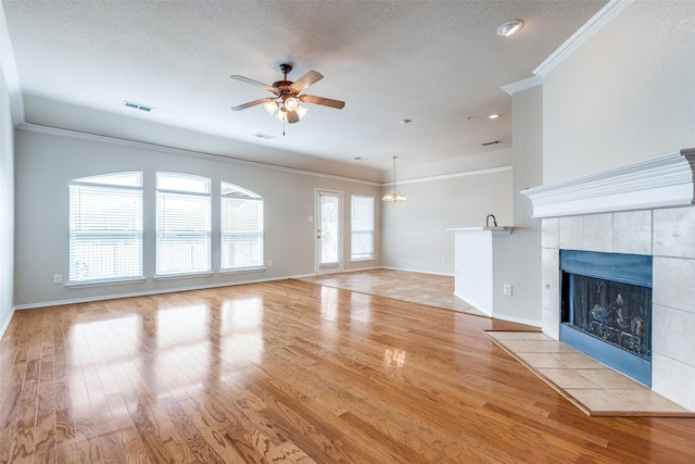 unfurnished living room featuring crown molding, visible vents, a tiled fireplace, wood finished floors, and ceiling fan with notable chandelier