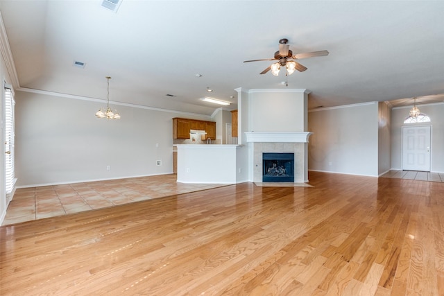 unfurnished living room with ceiling fan with notable chandelier, a fireplace, visible vents, ornamental molding, and light wood-type flooring