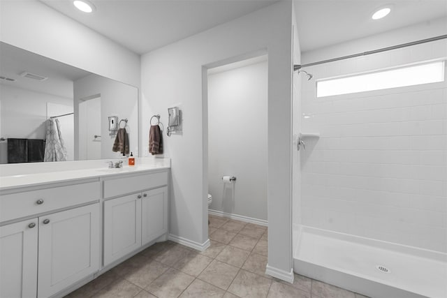 bathroom featuring toilet, a tile shower, vanity, tile patterned flooring, and baseboards