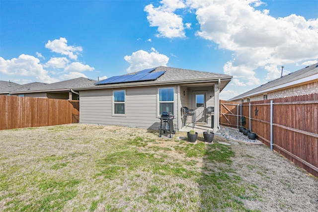 back of property featuring solar panels, a lawn, a fenced backyard, and roof with shingles