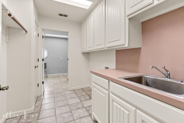 kitchen with baseboards, visible vents, light countertops, white cabinetry, and a sink