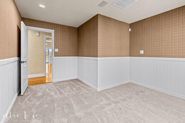 empty room featuring carpet, a wainscoted wall, visible vents, and wallpapered walls