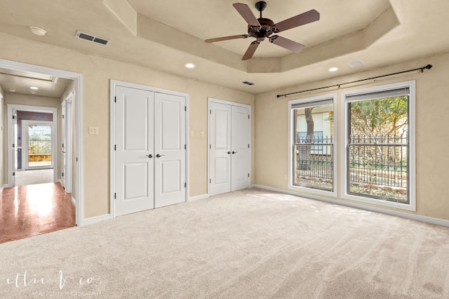 unfurnished bedroom with baseboards, visible vents, a tray ceiling, carpet floors, and two closets