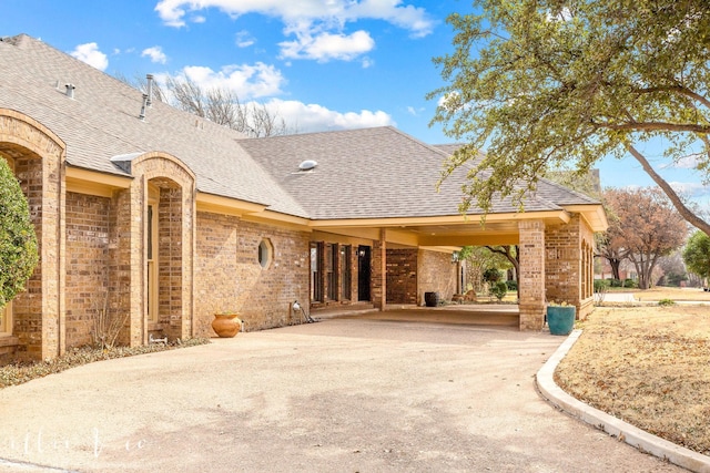 exterior space featuring brick siding, driveway, and roof with shingles