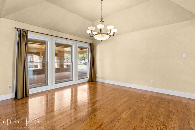 empty room with a notable chandelier, baseboards, vaulted ceiling, and wood finished floors