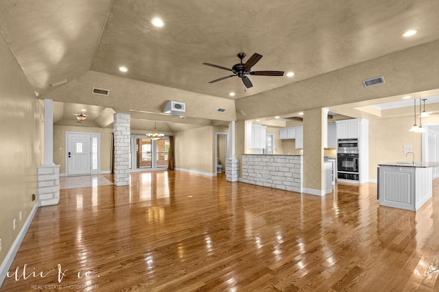 unfurnished living room featuring visible vents, a sink, light wood finished floors, and ornate columns