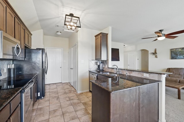 kitchen with decorative backsplash, a peninsula, arched walkways, stainless steel appliances, and a sink