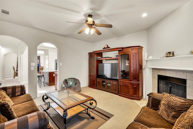 living area featuring arched walkways, visible vents, light carpet, ceiling fan, and a tile fireplace