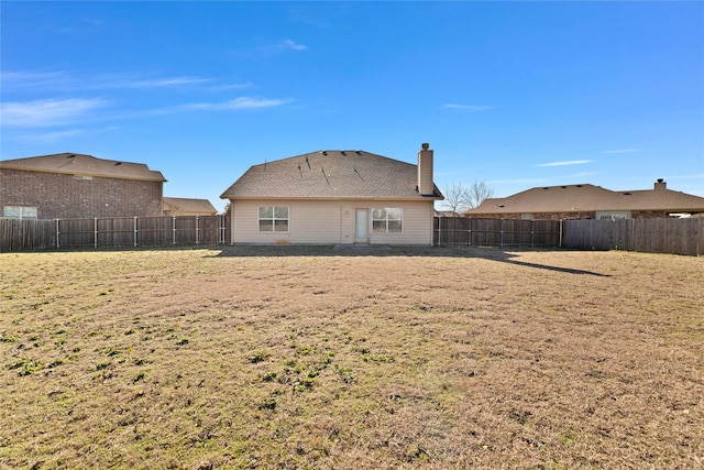 back of property featuring a chimney, a fenced backyard, and a lawn