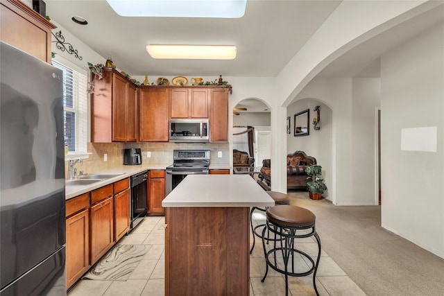 kitchen with arched walkways, decorative backsplash, appliances with stainless steel finishes, light carpet, and a kitchen bar