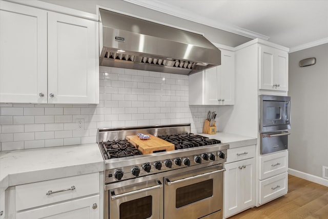 kitchen with a warming drawer, backsplash, appliances with stainless steel finishes, ornamental molding, and wall chimney range hood