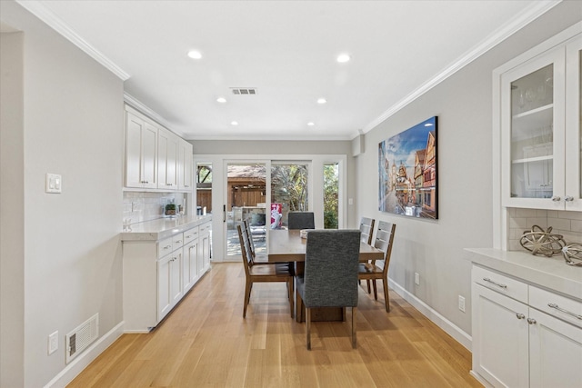 dining room featuring light wood-style floors, visible vents, crown molding, and baseboards