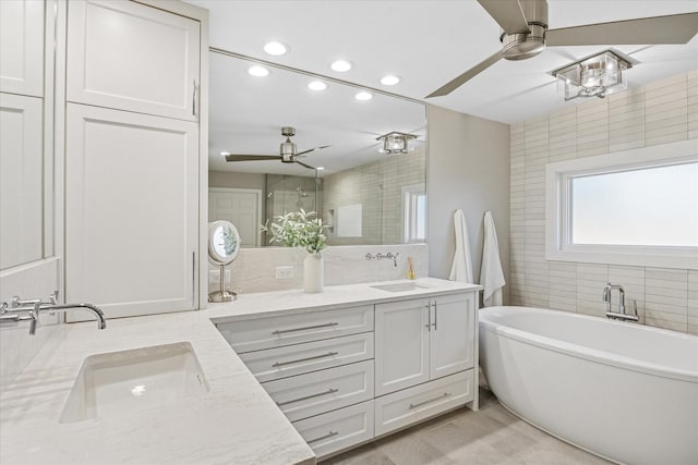 full bath featuring double vanity, a soaking tub, ceiling fan, and a sink