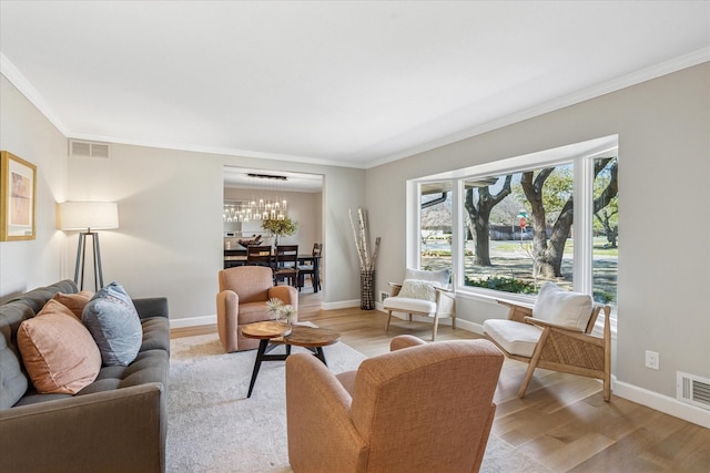 living area with ornamental molding, light wood-type flooring, visible vents, and baseboards