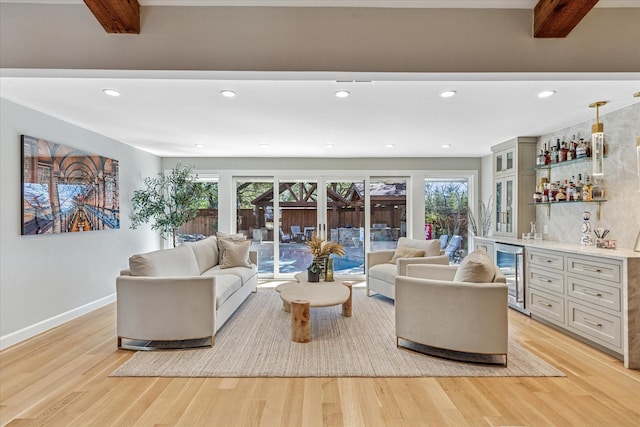 living area with beverage cooler, baseboards, wet bar, light wood finished floors, and beamed ceiling