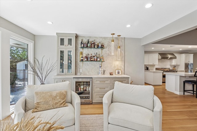 bar with beverage cooler, light wood-style floors, double oven range, decorative backsplash, and wall chimney exhaust hood