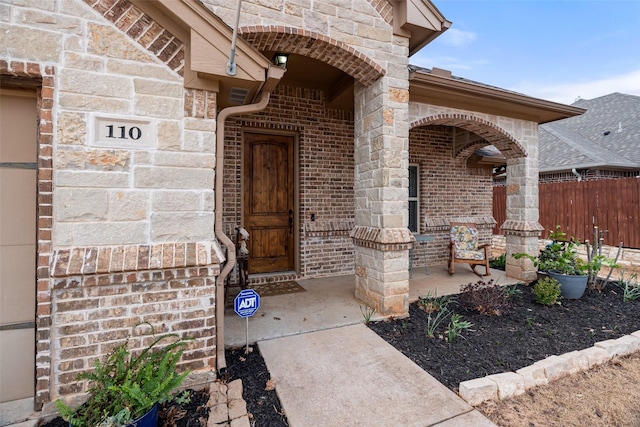 entrance to property featuring brick siding, a porch, and fence