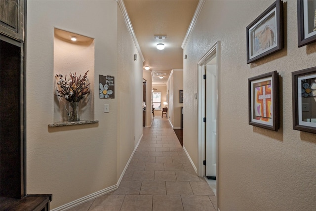 hall featuring baseboards, crown molding, and tile patterned floors