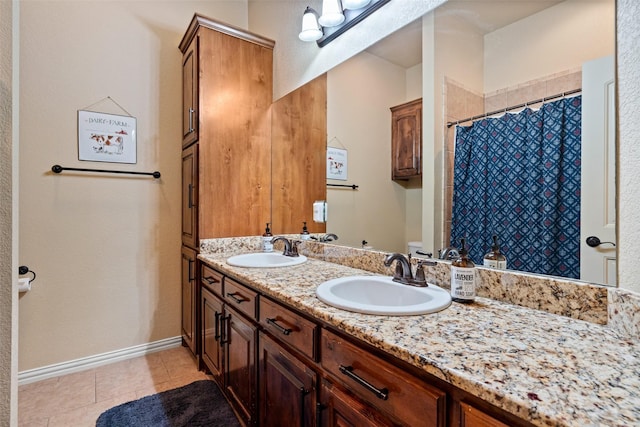 full bath featuring double vanity, tile patterned flooring, a sink, and baseboards