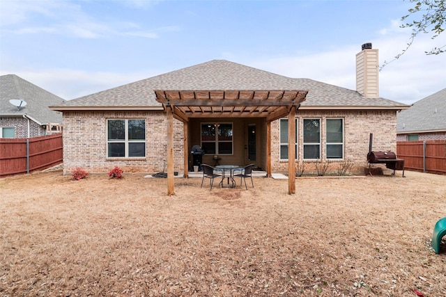 back of house featuring brick siding, a chimney, a fenced backyard, and a pergola