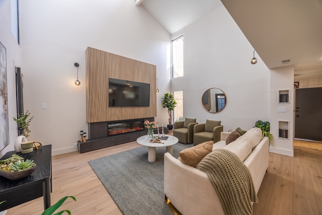 living room featuring a wealth of natural light, a high ceiling, a glass covered fireplace, and light wood finished floors