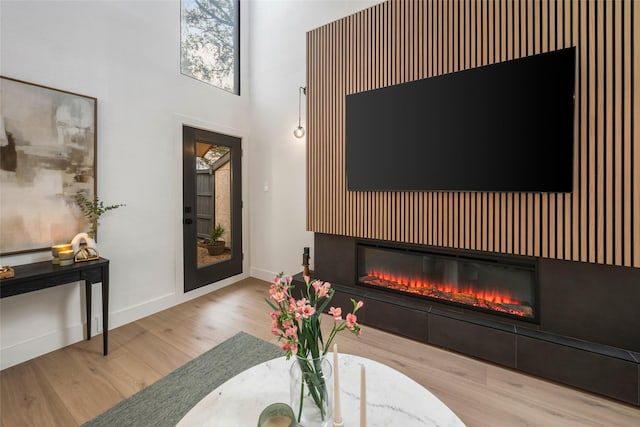 living room featuring a glass covered fireplace, baseboards, wood finished floors, and a towering ceiling