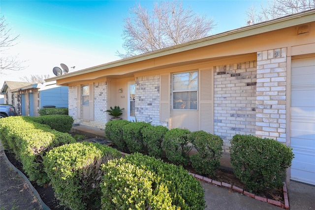 doorway to property featuring a garage and brick siding