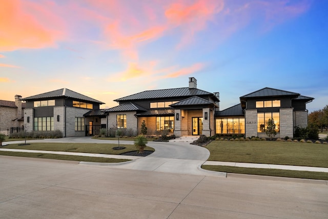 prairie-style home with a standing seam roof, curved driveway, a chimney, stone siding, and metal roof