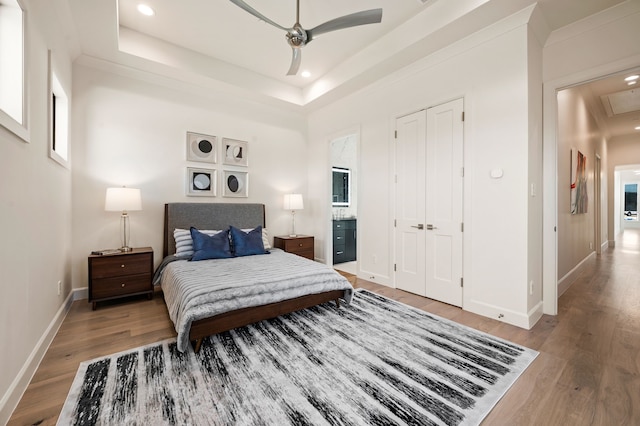 bedroom featuring light wood finished floors, baseboards, a tray ceiling, recessed lighting, and a ceiling fan