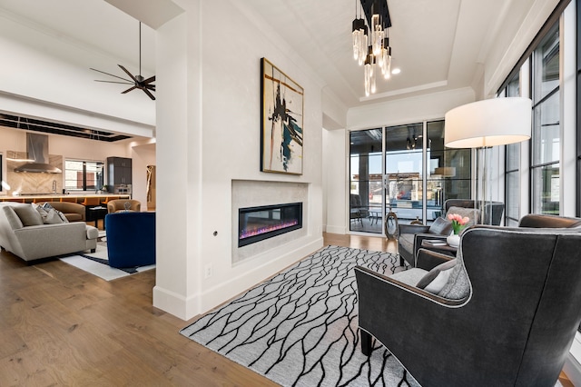 living room with a glass covered fireplace, baseboards, wood finished floors, and ceiling fan with notable chandelier