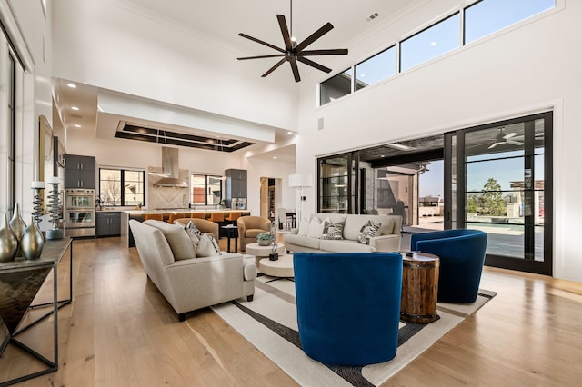 living area with visible vents, light wood-style floors, ceiling fan, and ornamental molding