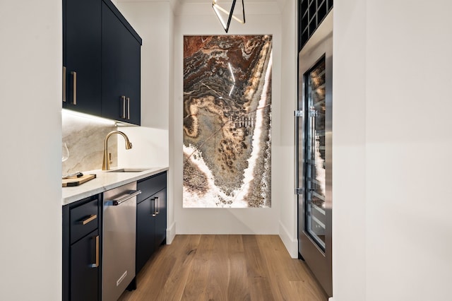 bar featuring light wood-type flooring, a sink, stainless steel dishwasher, backsplash, and wine cooler