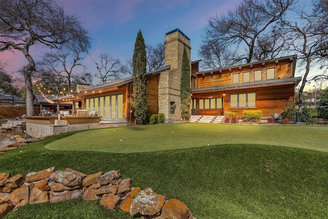 back of property at dusk with a chimney and outdoor dry bar