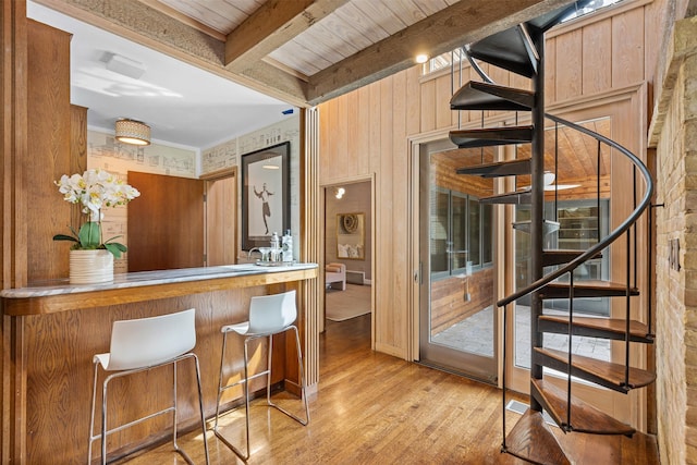 bar featuring indoor bar, beamed ceiling, light wood-style flooring, and stairs