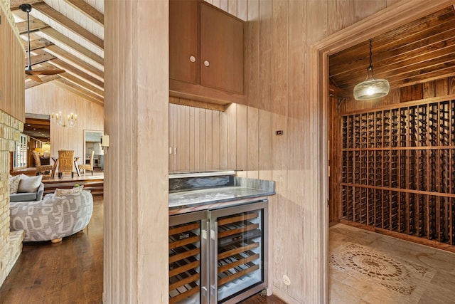 wine area featuring beverage cooler, wooden walls, wood finished floors, vaulted ceiling, and a chandelier