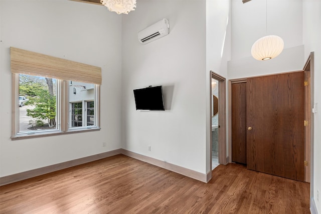 interior space featuring a wall mounted air conditioner, wood finished floors, a towering ceiling, and baseboards