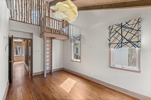 empty room featuring a high ceiling, baseboards, wood finished floors, and beamed ceiling