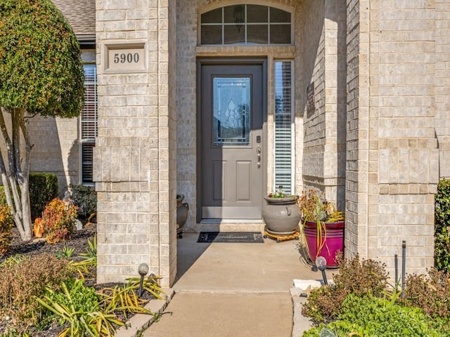 doorway to property with a shingled roof and brick siding